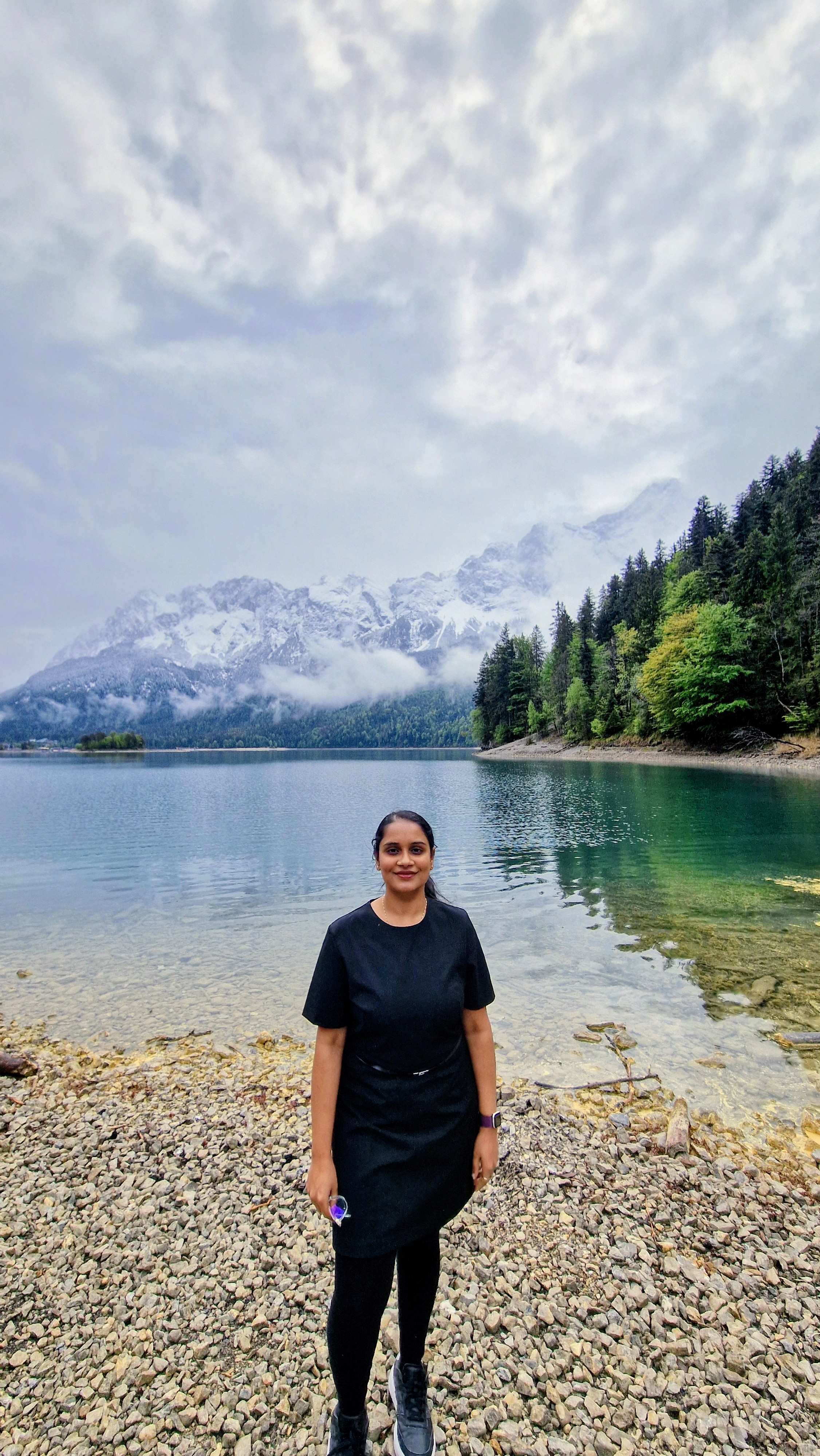 Pramodini Subramanya by a clear alpine lake with snow-capped mountains behind her.